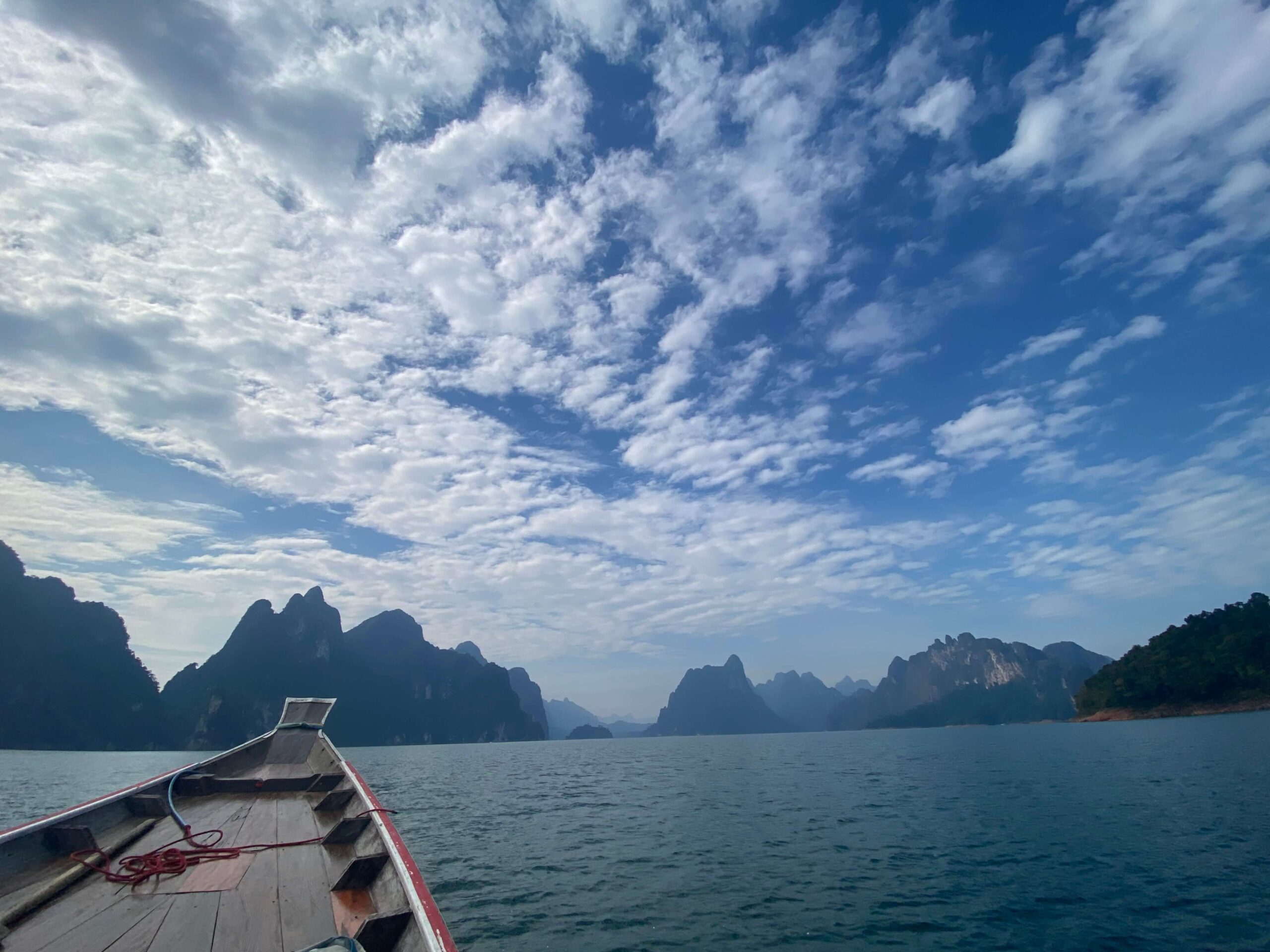 longtail boat in water with mountains in the distance - beautiful places in thailand