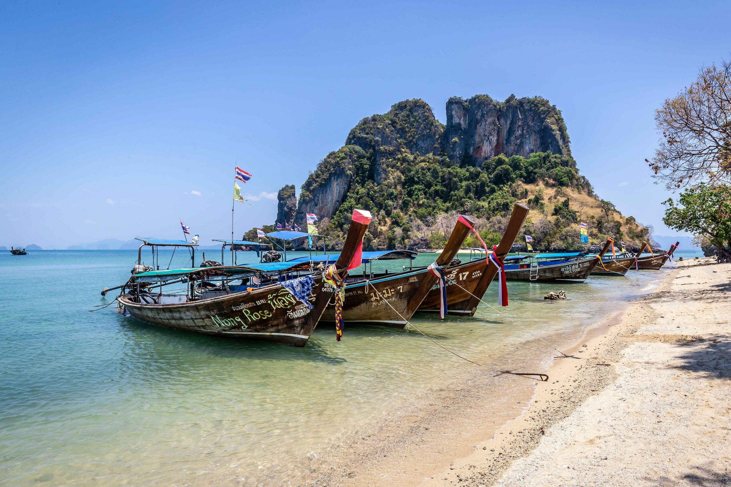 long tail boats parked on the sand in the ocean with limestone cliffs in the back